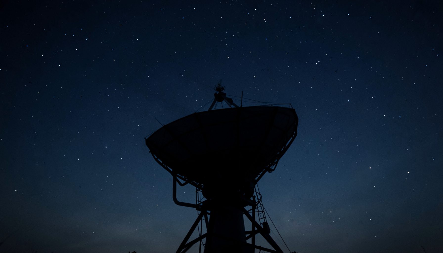 A satellite dish silhouetted against a deep twilight sky with scattered stars, dark blue and charcoal tones dominating