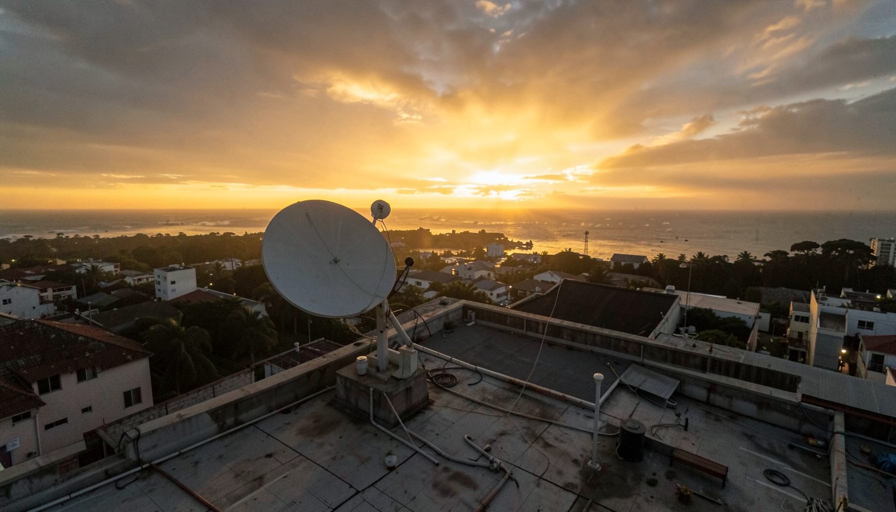 Aerial view of a rooftop with a satellite dish pointing toward a golden sunset sky, warm amber and charcoal tones