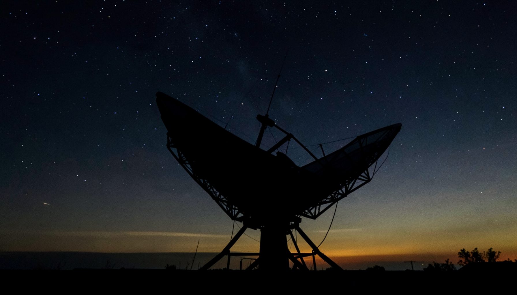 Dark night sky with a satellite dish silhouette against a faint glow of stars, deep navy and charcoal tones