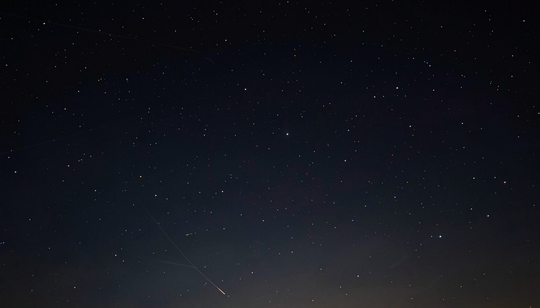 Night sky with scattered stars and a faint satellite trail crossing the darkness, deep navy and charcoal tones with subtle glow